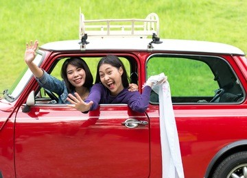 two travel woman in car road trip waving out the window smiling