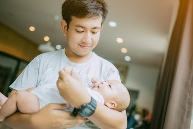 portrait of young asian father holding his newborn baby son at home.