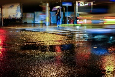 rainy night in the big city, light from the shop windows reflected on the road on which cars travel. view from the level of asphalt.