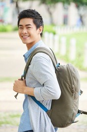 handsome college student with backpack standing in profile and looking at camera with toothy smile, waist-up portrait