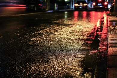 rainstorm night in the big city, light from the shop windows reflected on the road on which cars travel. view from the level of asphalt.