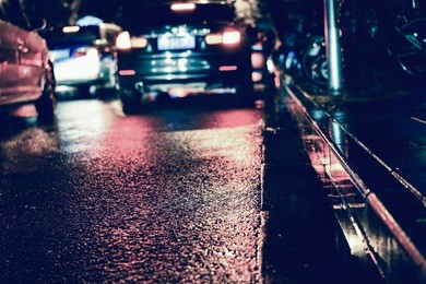 rainstorm night in the big city, light from the shop windows reflected on the road on which cars travel. view from the level of asphalt.