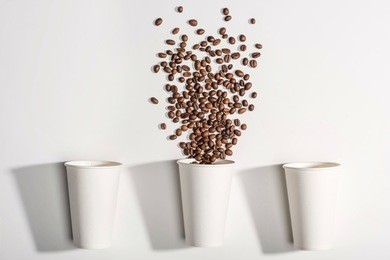 top view of white disposable paper cups with coffee beans isolated on white