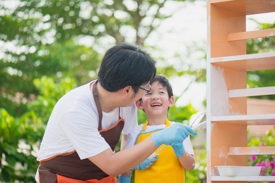 asian father and son painting wooden shelf together