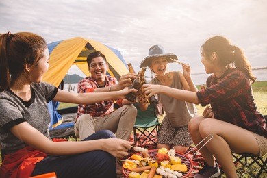group of friends drinking beer in camping, people in asian are celebrating the festival they clink glass bottles beer and dinner happy,