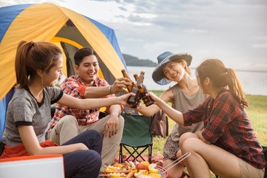 group of friends drinking beer in camping, people in asian are celebrating the festival they clink glass bottles beer and dinner happy,