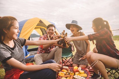group of friends drinking beer in camping, people in asian are celebrating the festival they clink glass bottles beer and dinner happy,