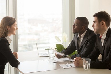 side view of female applicant introducing herself during job interview, talking about working experience, multiracial recruiters hr managers interviewing listening to candidate, considering cv resume