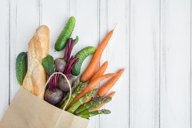 paper shopping bag with fresh bread, carrots, cucumbers, asparagus and beet. eco shopping concept, products for cooking. flat lay on white vintage wooden table. top view with place for text