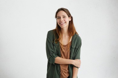 gorgeours young european woman with healthy clean skin and beautiful set of features, dressed in dark-green shirt over brown top, wearing her hair loose, looking at camera with shy charming smile