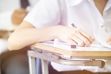 soft focus front view undergraduate student holding pencil and sitting on row chair doing final exam attending in examination room or classroom.university student in uniform.