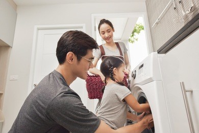 happy family loading clothes into washing machine in home