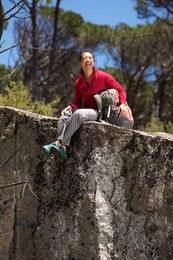 portrait of cheerful asian female hiker sitting at the edge of mountain and laughing