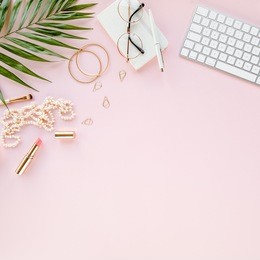 office table desk with computer,  green leaves palm, clipboard. magazines, social media. top view. flat lay. home office workspace. women's fashion accessories isolated on pink background. 