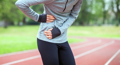 athletic woman on running track has side cramps during workout