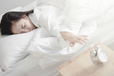 asian girl trying to get up from bed in the morning. reach for bedside alarm clock.