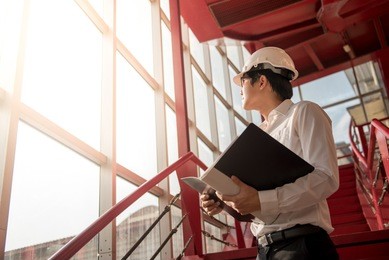 young asian engineer or architect holding files while wearing personal protective equipment safety helmet at construction site. engineering, architecture and building construction concepts