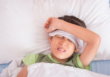 little boy had high fever with towel over his head laying in the bed