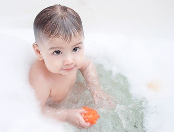 cute baby is swimming in bath in a foam
