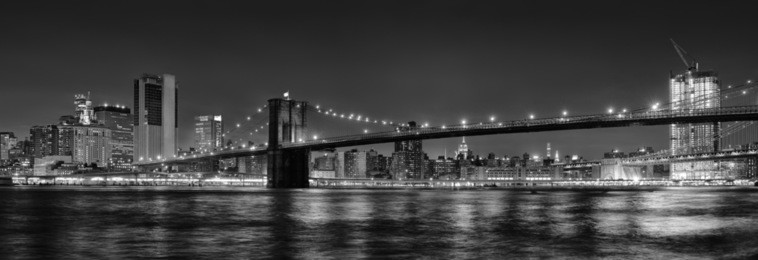 black and white panoramic photo of brooklyn bridge at night, new york city, usa.
