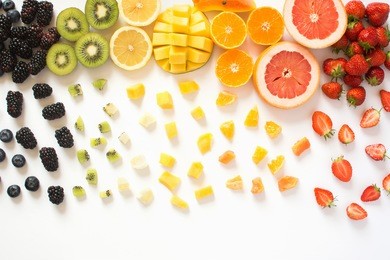 overhead view of whole fruits and cut slices in the rows, red, orange, yellow, green fruits with cut pieces on the white background, grapefruit, mango, strawberries, orange, lemon, kiwi
