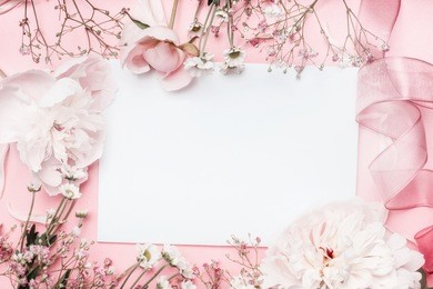 white blank card with pastel flowers and ribbon on pink pale background, floral frame. creative greeting, invitation and holiday concept