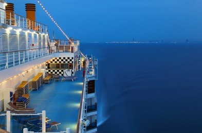 illuminated cruise ship with people in the sea at night near city