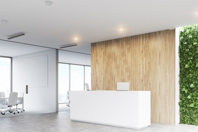 corner of a white reception desk with two laptops standing on it in front of a wooden office wall. there is a grass wall seen through a wall opening. 3d rendering, mock up