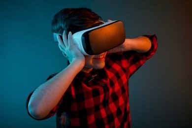 smiling kid in checkered shirt posing while wearing vr goggles on studio background. 