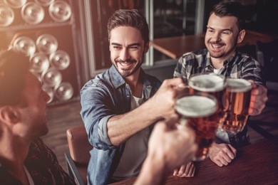 cheers, my friends! three handsome men are drinking beer, celebrating meeting and smiling.