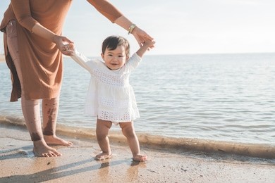 portrait of a mother help her daughter by holding her hand walking on the beach for the first time