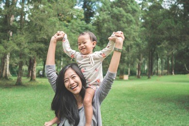 portrait of happy baby girl sitting on mom's shoulder in the park