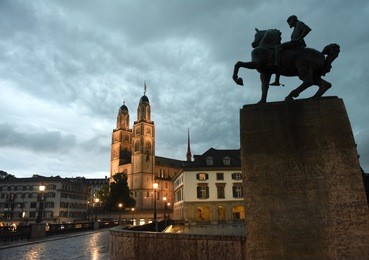 zurich evening view on great minster church (grossmunster) and hans waldmann monument, zurich, switzerland 