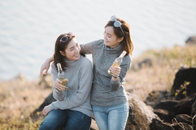 summer, holidays, vacation, happy people concept - smiling asia girlfriends with bottles of beer or non-alcoholic drinks,flare light