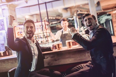 handsome businessmen are sitting on a bar counter, drinking beer and watching football. active fans.