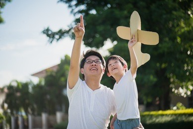 asian father and son playing cardboard airplane together in the park outdoors