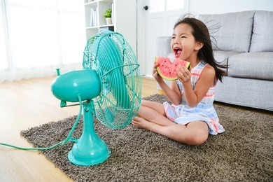 beautiful youth girl holding watermelon sitting in front of electric fan and blowing cool fan for eliminating summer hot.
