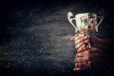 low key image of a man holding a trophy cup over dark background with glitter overlay