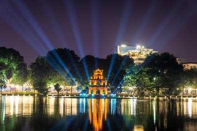 night view of the hoan kiem lake (lake of the returned sword) and the turtle tower among blue light rays at historic centre of hanoi in vietnam. the tower reflected in the lake.