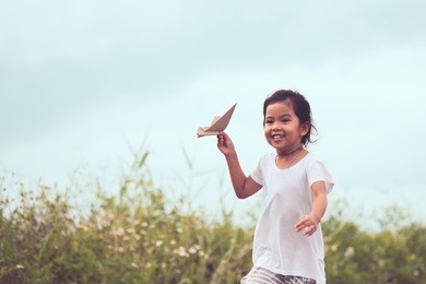 cute asian child playing toy paper airplane in the meadow in vintage color tone