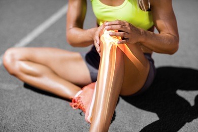 low section of sportswoman suffering from knee pain while sitting on track during sunny day