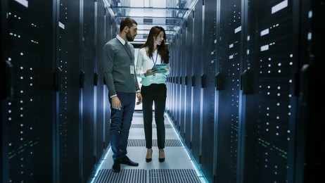 female and male it engineers discussing technical details in a working data center/ server room.