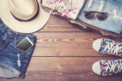 travel preparations with casual summer clothes on wooden table. top view
