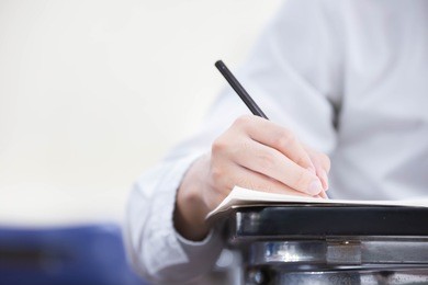 front view undergraduate student holding pencil.sitting on lecture chair doing final exam attending in examination room or study in classroom.university student in uniform.space for text.