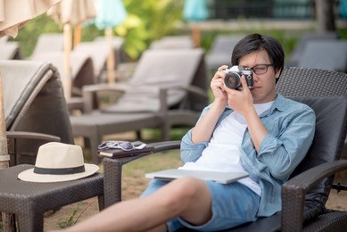 young asian man taking photos on bench near the beach, summer holiday and vacation travel concepts