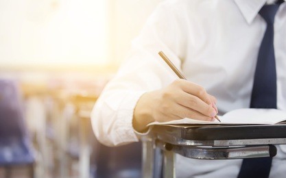 front view undergraduate student holding pencil.sitting on row chair doing final exam in examination room or study in classroom.university student in uniform.space for text.