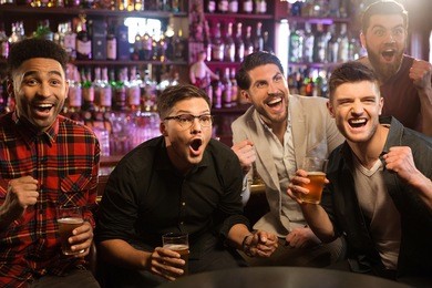 happy friends having fun in pub by watching sport on tv together while drinking beer and cheering for team