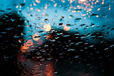 textures of water droplets of rain flow down the windowpane. rain drop on the car glass background, night city life through windshield, lights and rain.