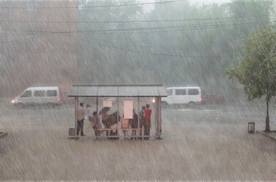 crowd of people are hiding from heavy rain at a stop in the city