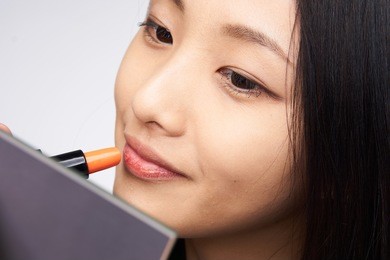 woman is painting lipstick, woman with lipstick, woman is looking in mirror on light background portrait.